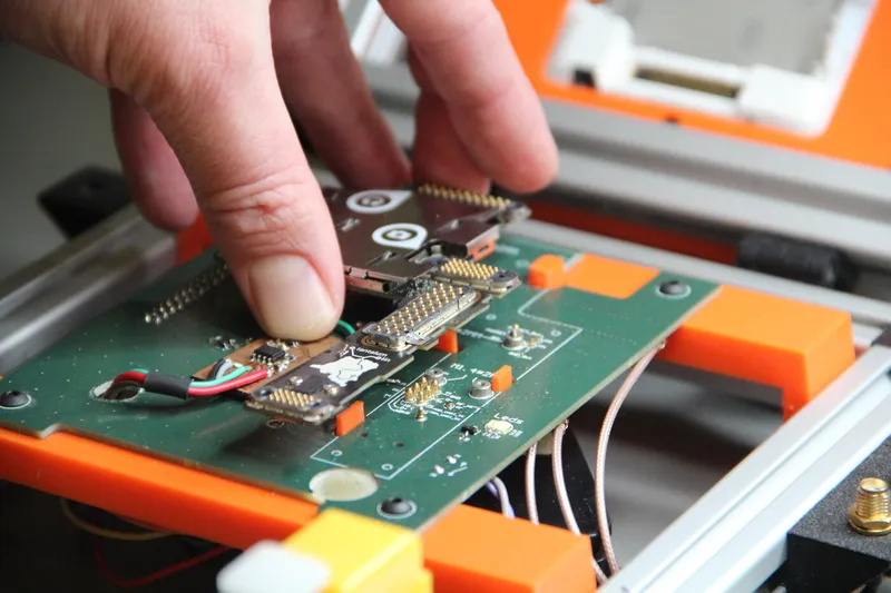A mainboard pressed by hand onto a test fixture, its contacts meeting the pins of the green probe board