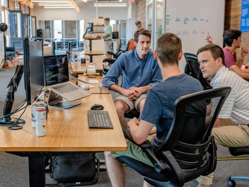 Team of guys talking around a desk with a computer